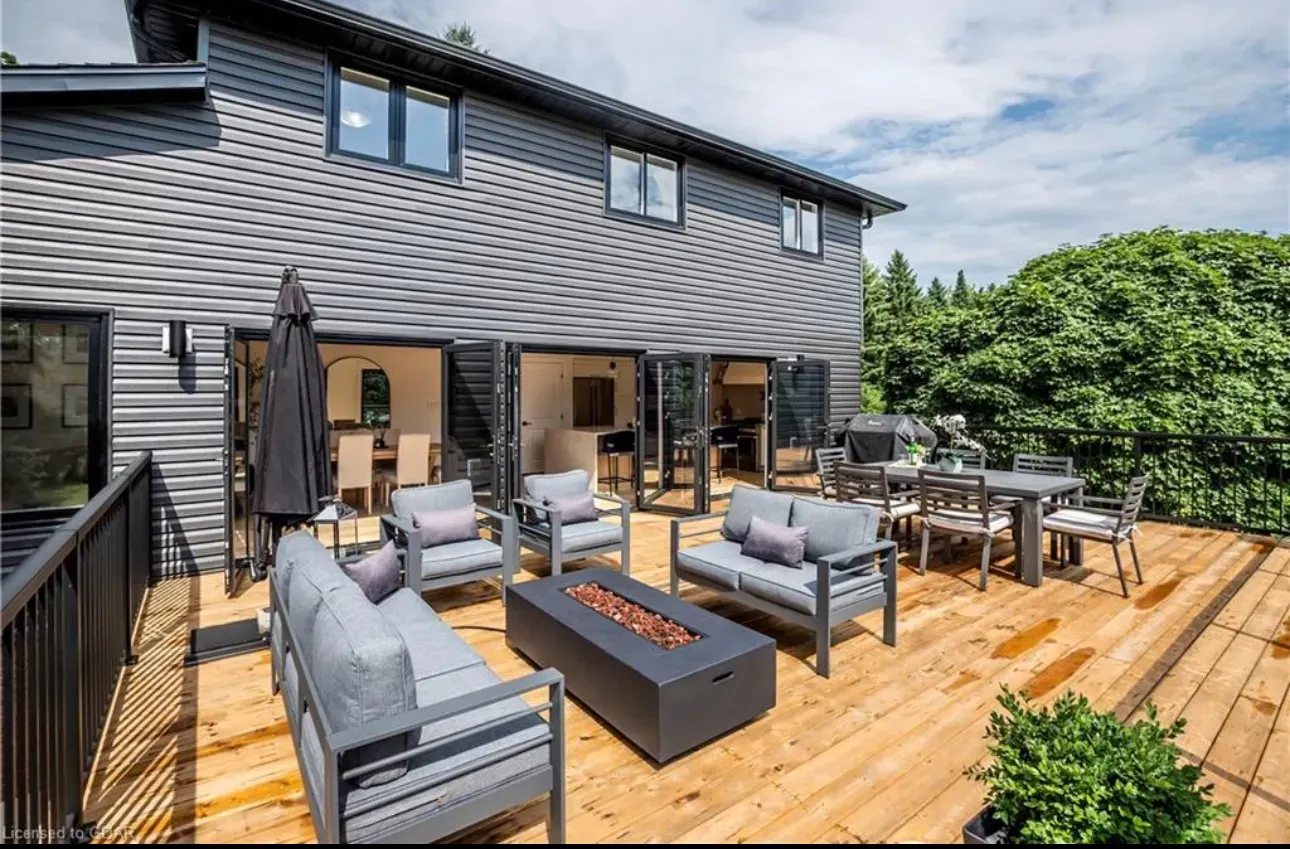 Outdoor deck with gray furniture, a fire pit, and a dining table, connected to a dark gray house.