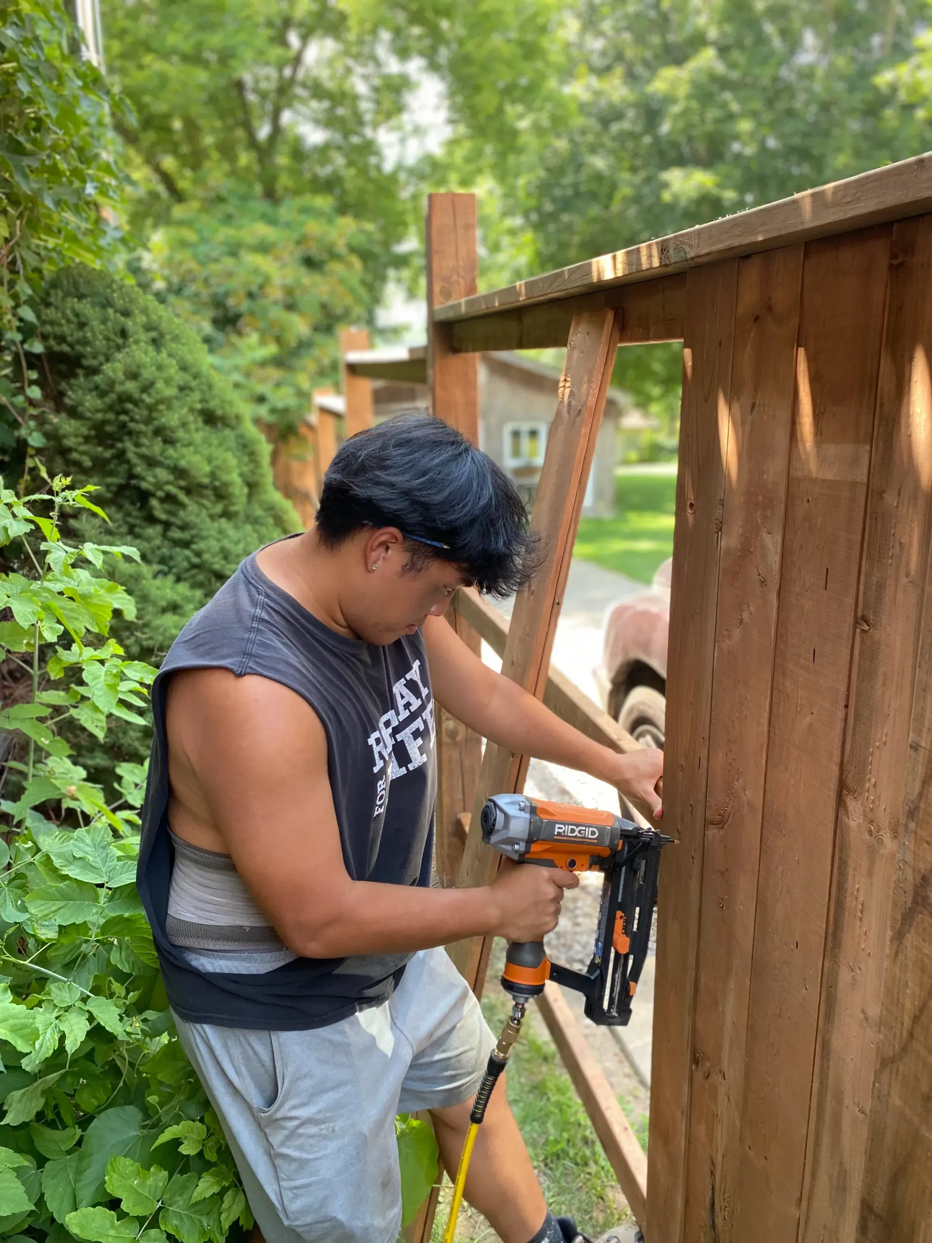 Person using a nail gun to construct a wooden fence outdoors.