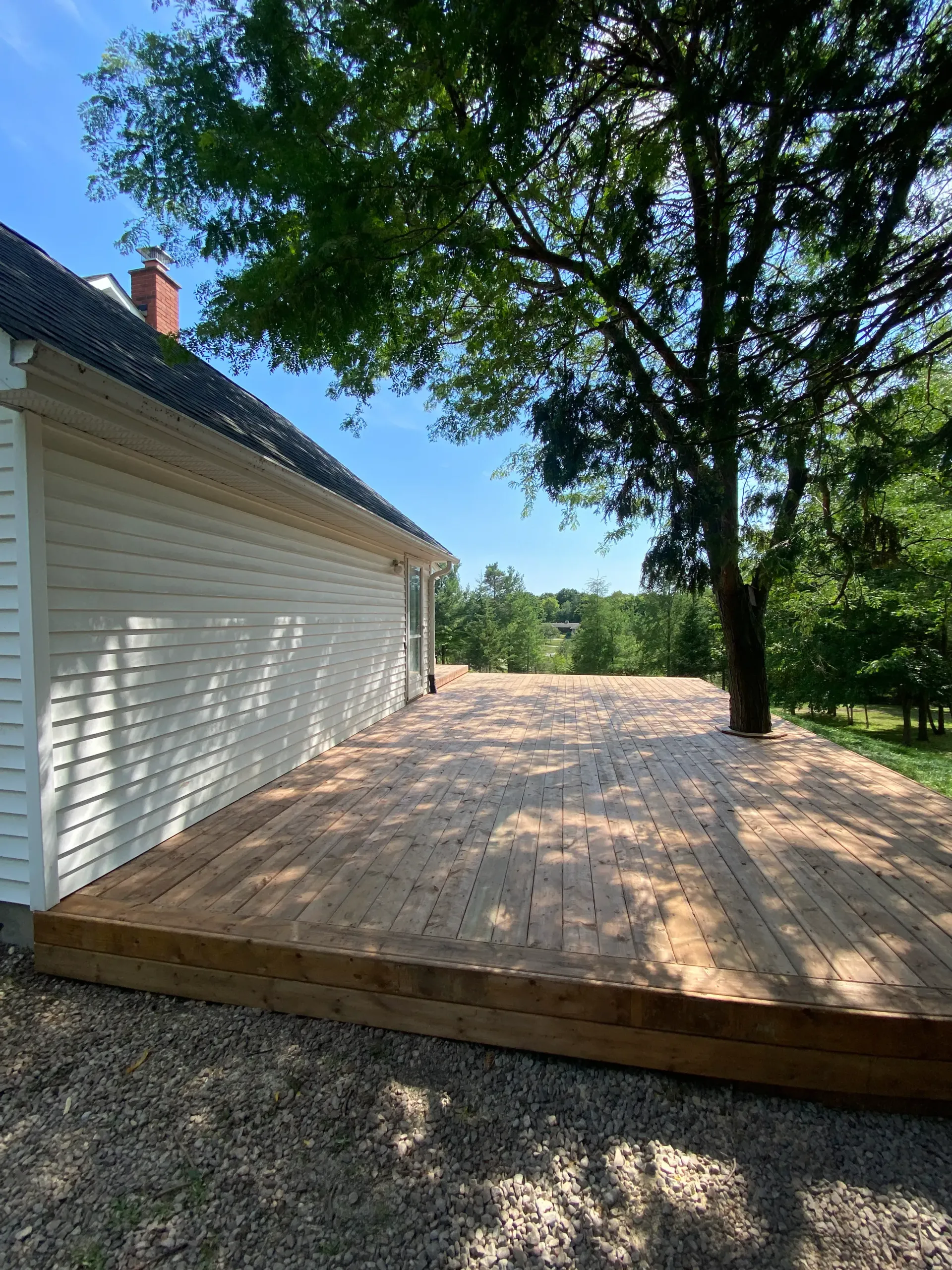 Wooden deck next to a white building and tree, under a blue sky.