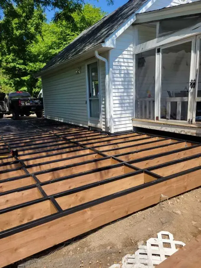 Partially constructed wooden deck next to a white house with a screened porch. Brown wood and black metal supports.