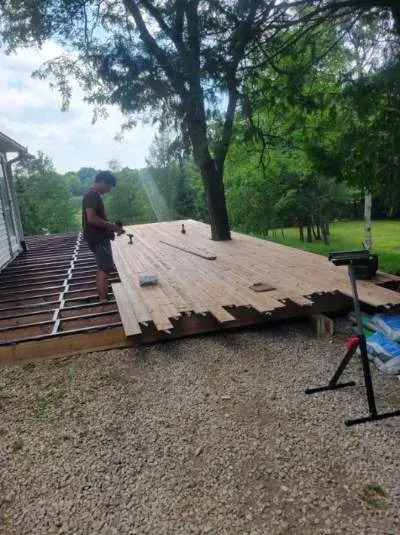 Person builds a deck attached to a house, partially completed, with a tree growing through it.