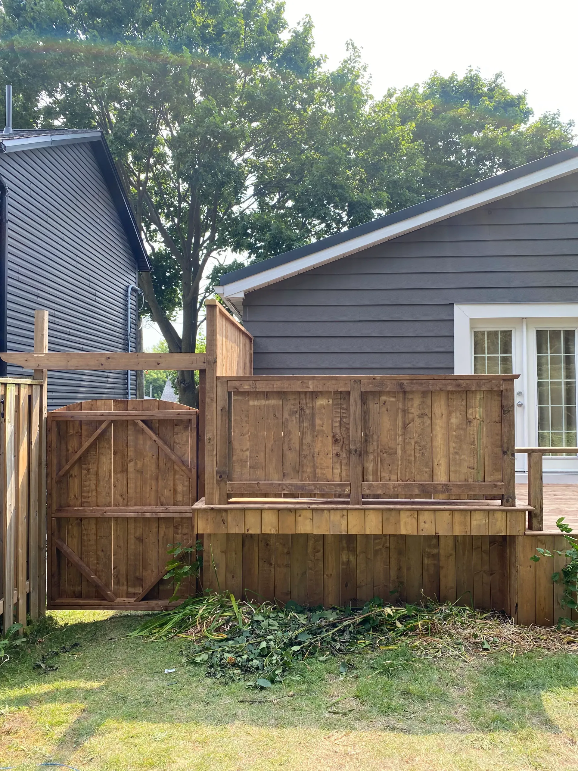 Wooden deck with a gate and fence, next to a house with gray siding.