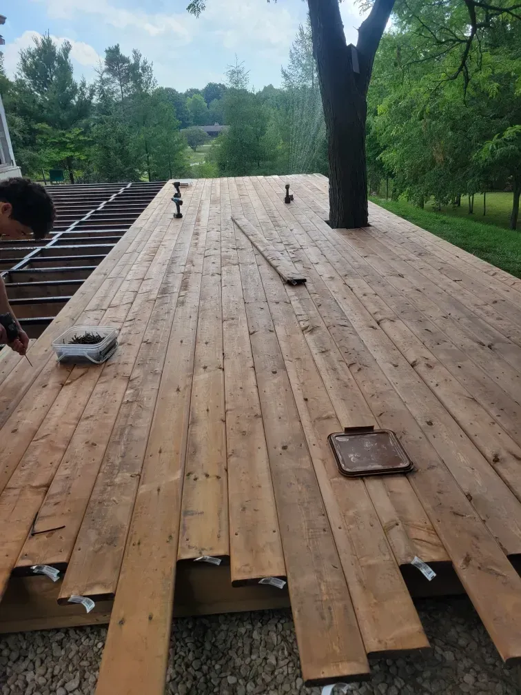 Deck being rebuilt; weathered wooden planks, tree, and person working outdoors.