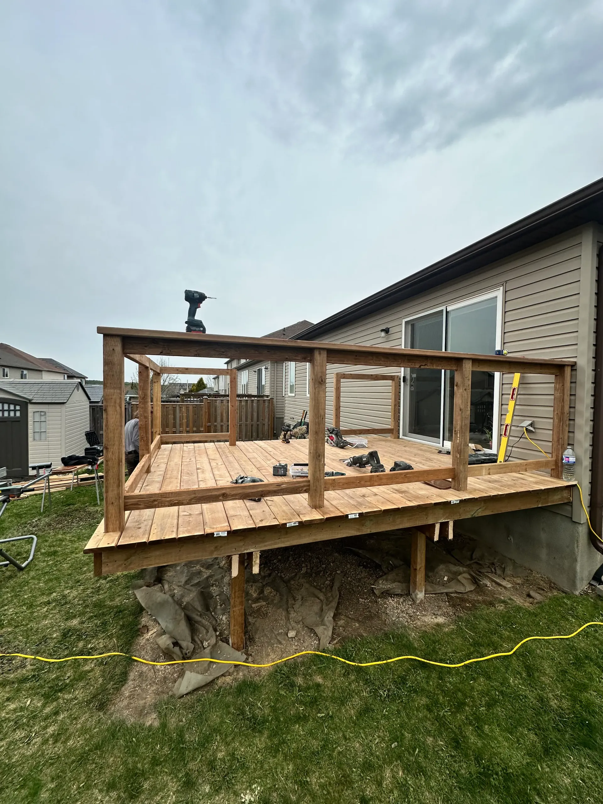 Wooden deck being built next to a beige house, with railings and a cloudy sky.