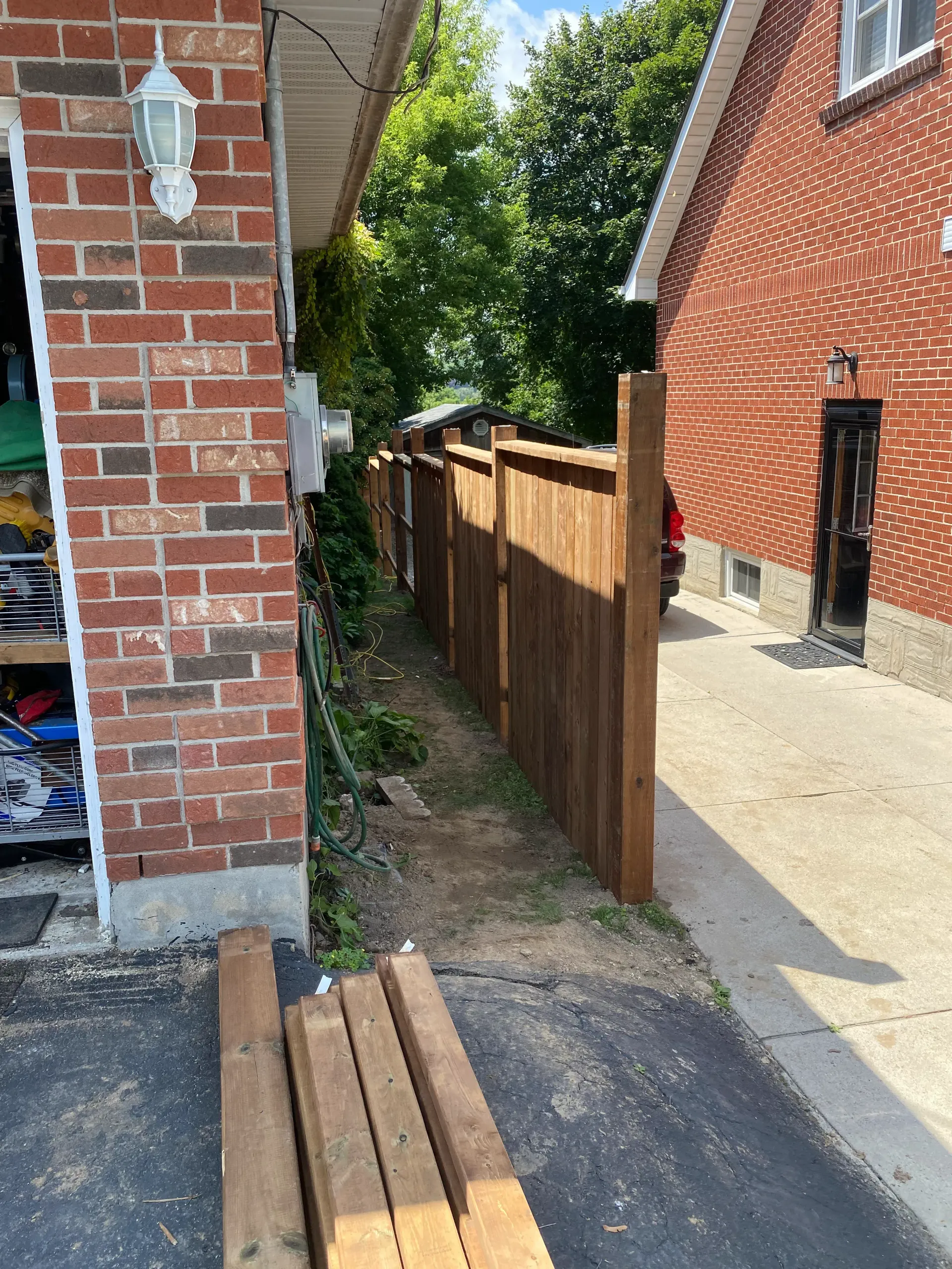 A narrow space with a brown fence between a brick building and a red brick building.