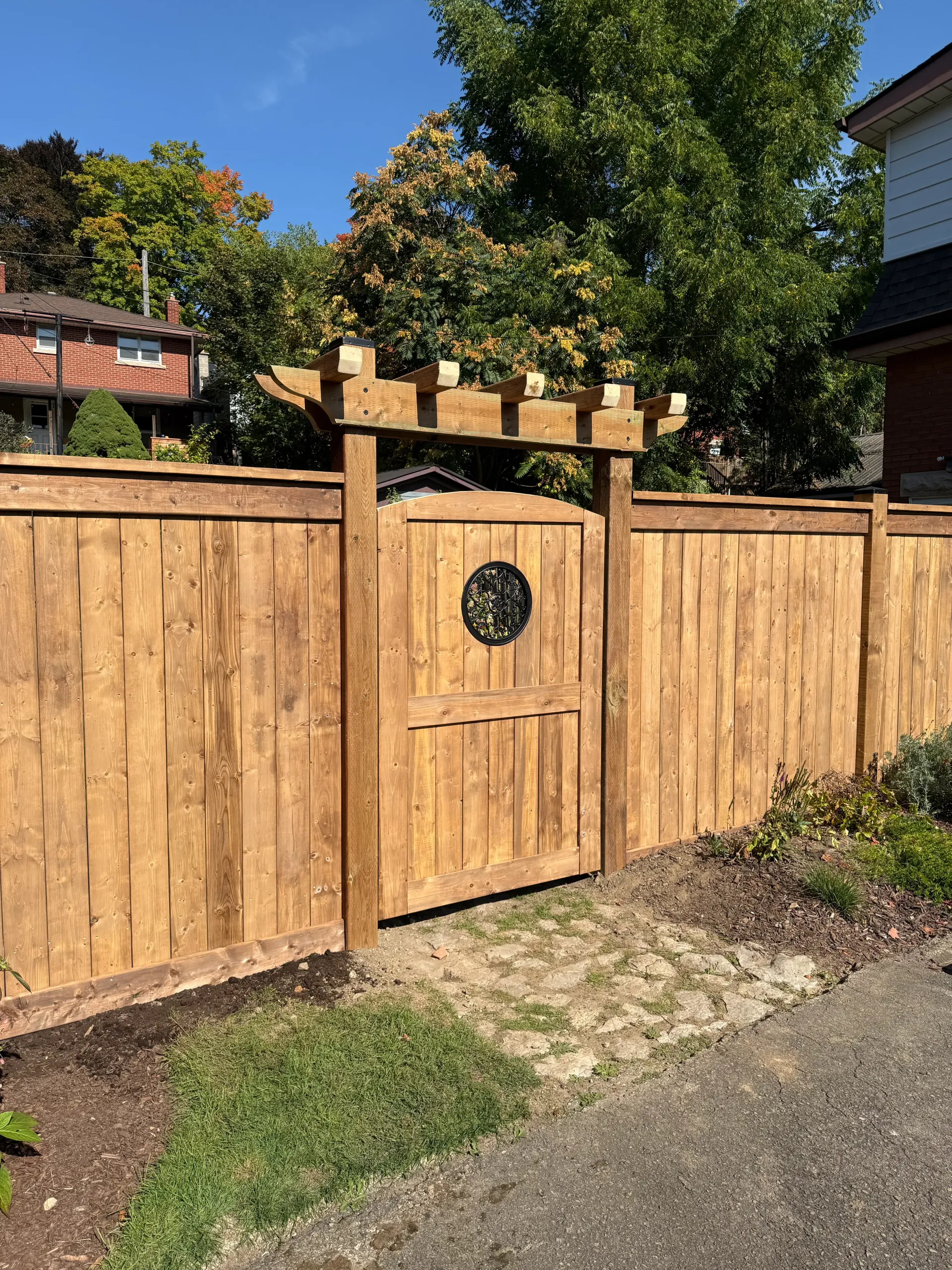Wooden fence with gate, arched trellis, and brick path in front.