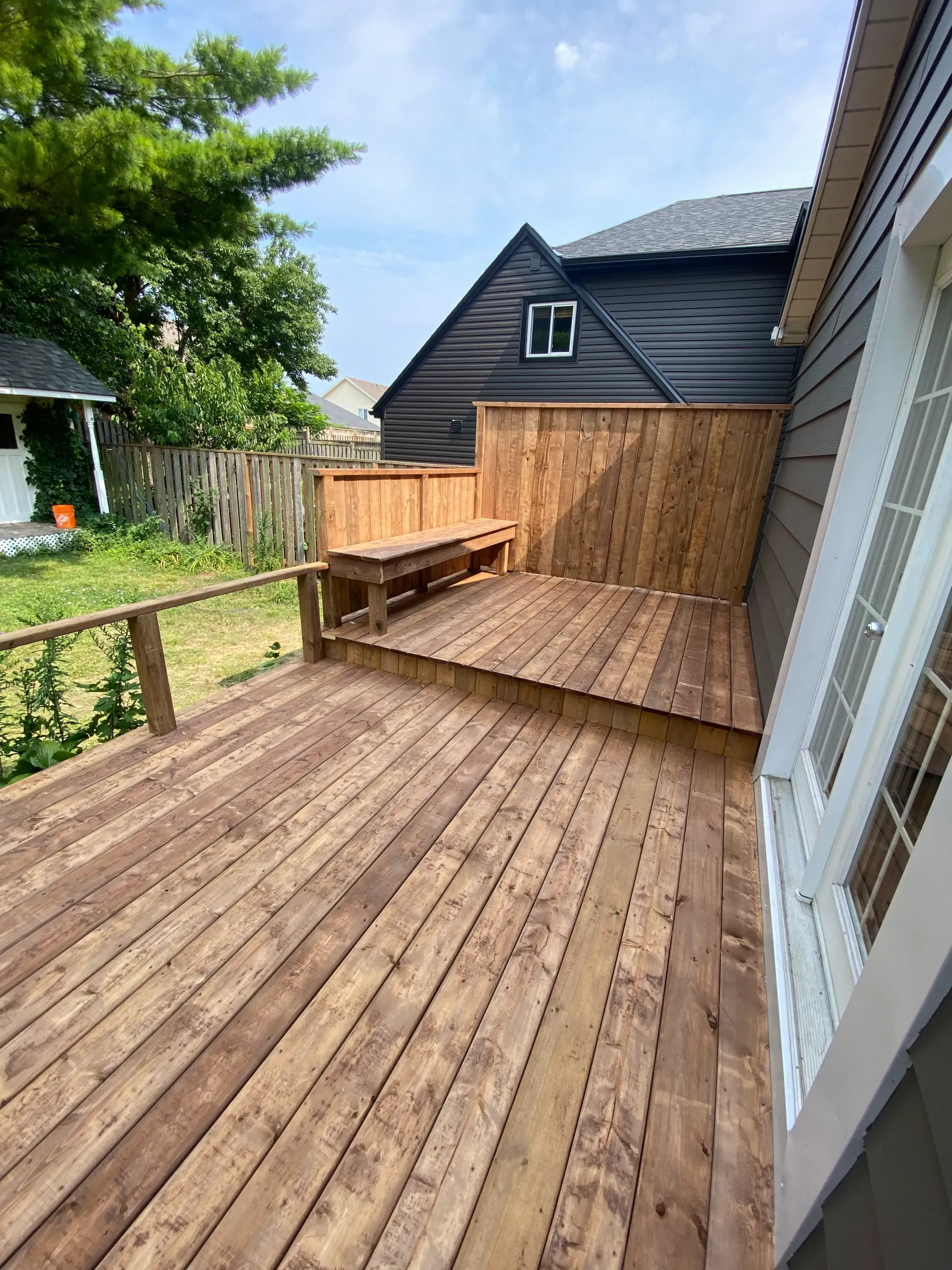 Wooden deck with built-in bench and privacy fence next to a house with black siding.