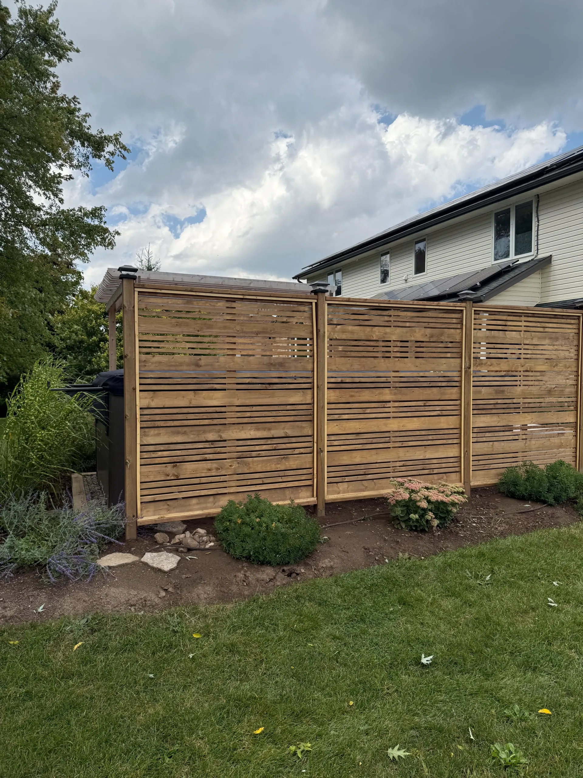Wooden privacy fence in a yard with grass and house in background.