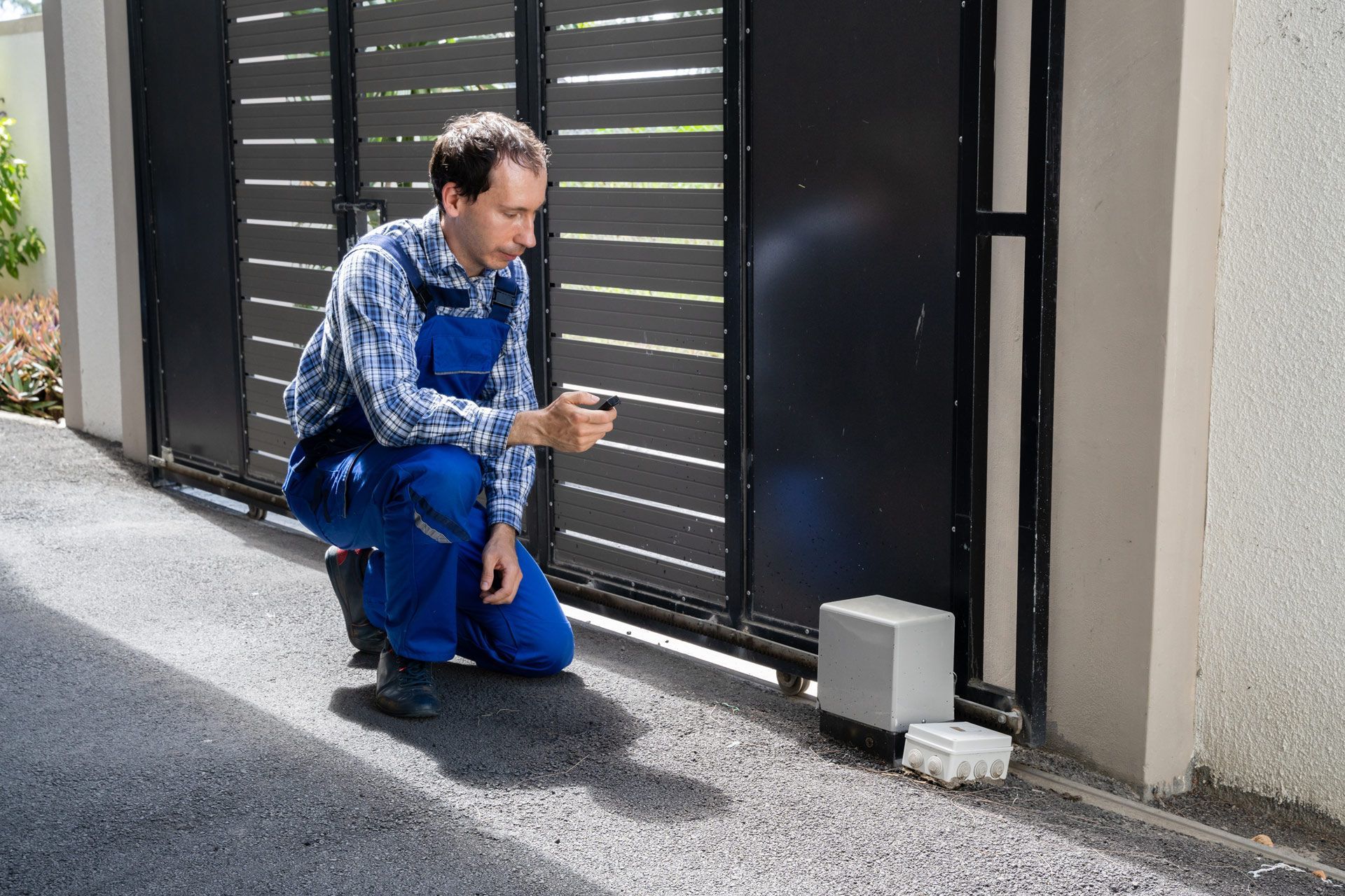 A man is kneeling down next to a sliding gate and looking at a cell phone.