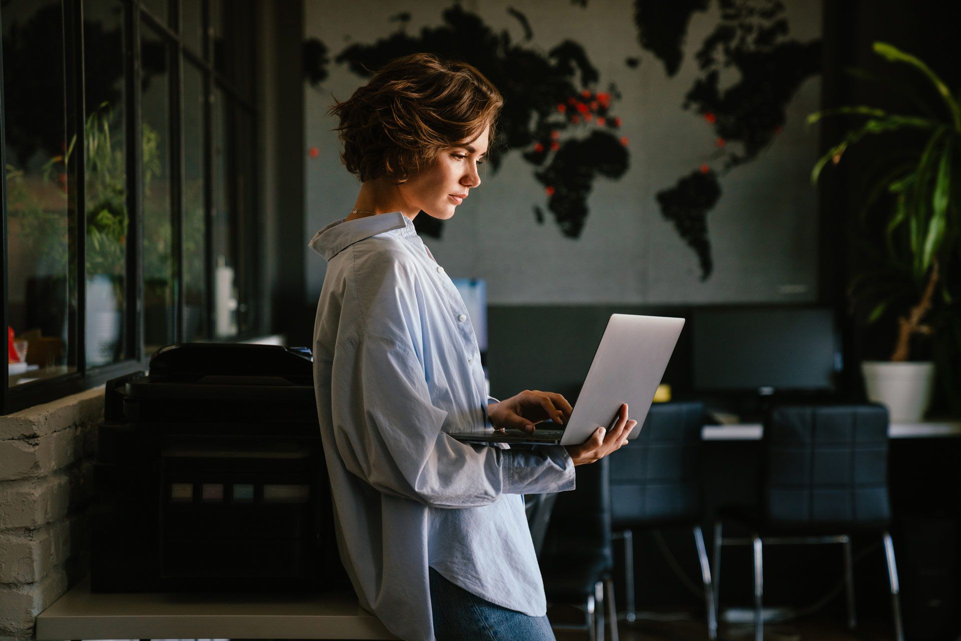 A woman is standing next to a table using a laptop computer.