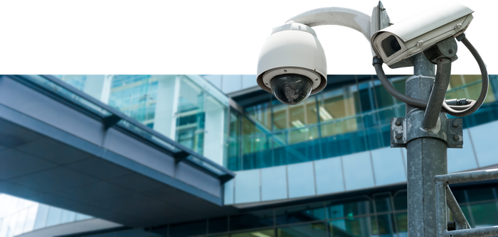 A security camera is sitting on a pole in front of a building.