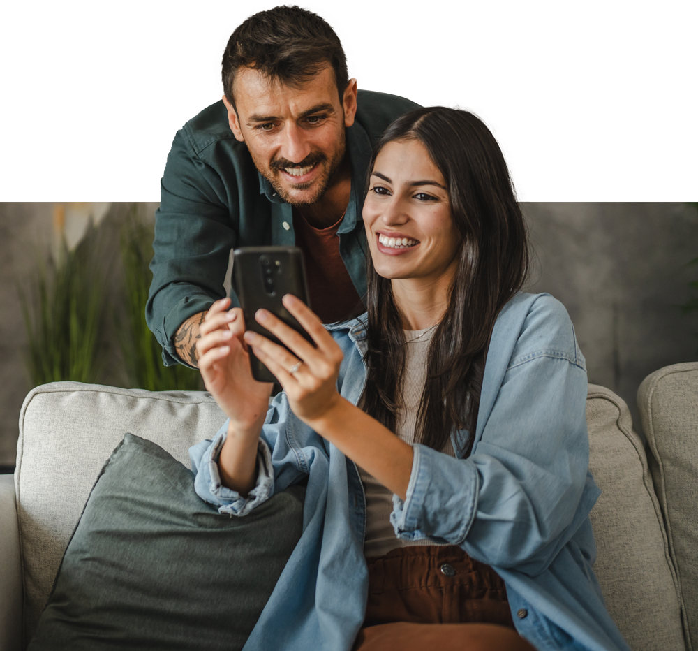 A man and a woman are sitting on a couch looking at a cell phone.