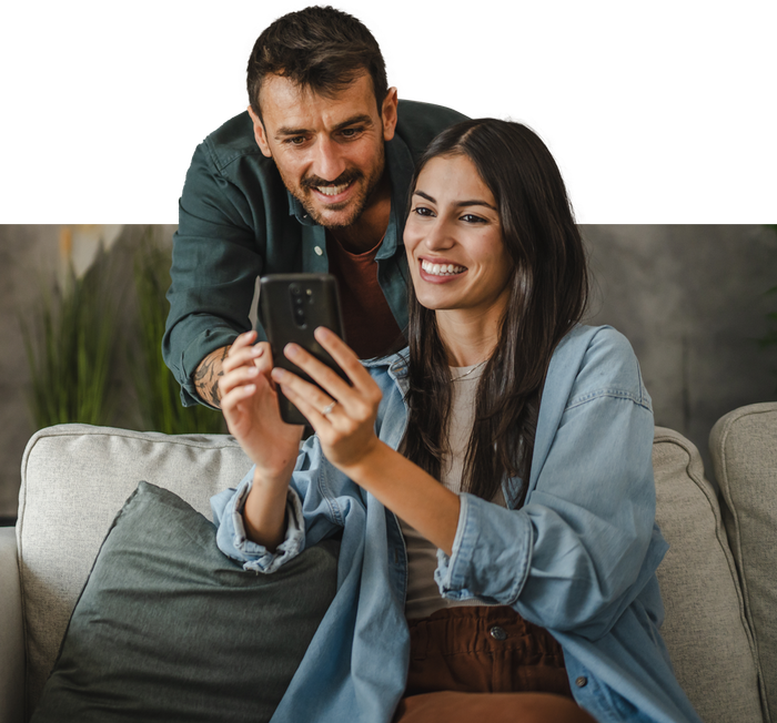 A man and a woman are sitting on a couch looking at a cell phone