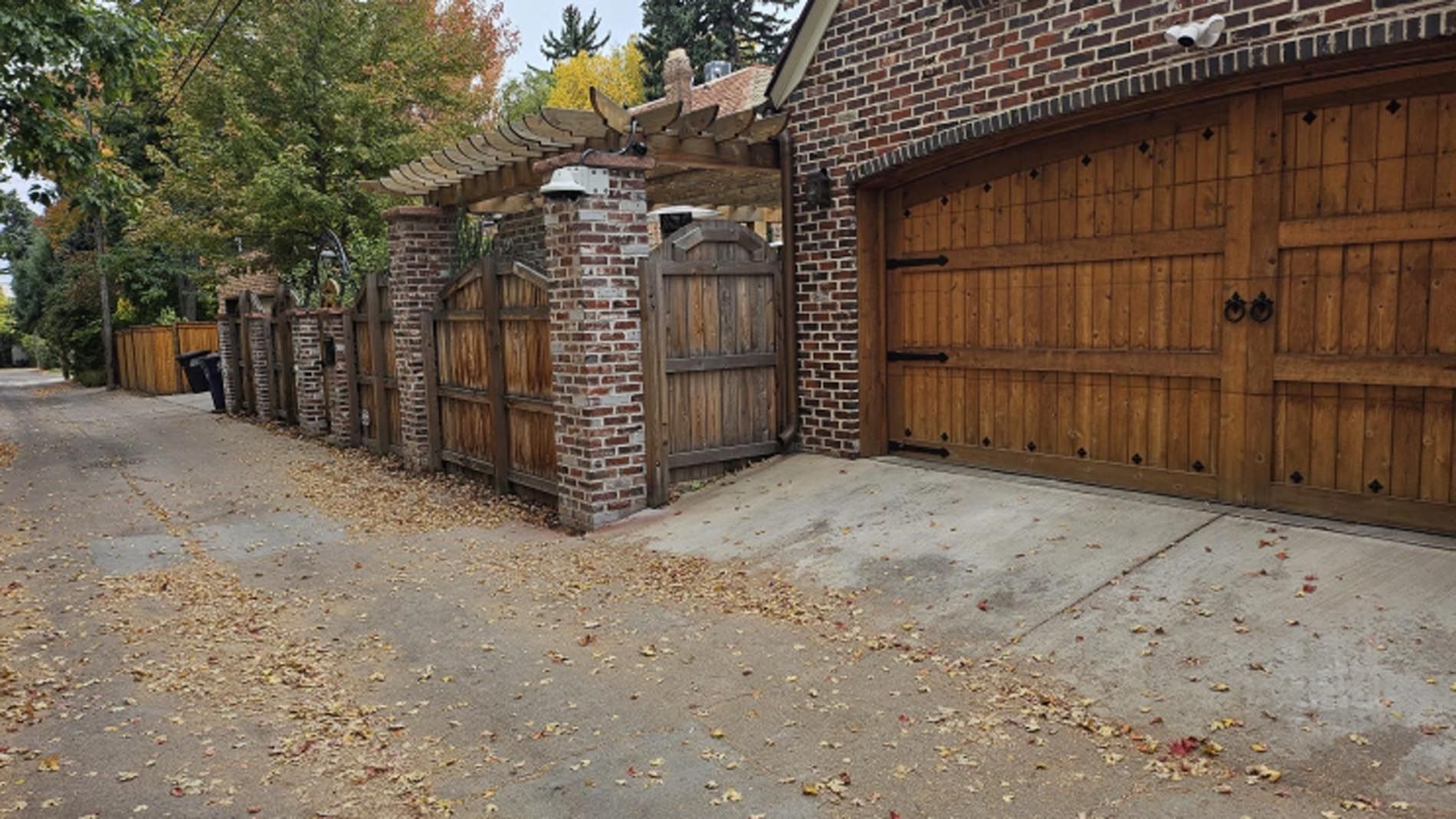 A brick garage with wooden doors and a wooden fence surrounding it.