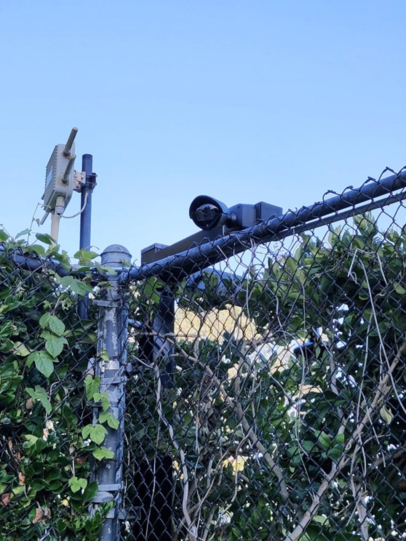 A security camera is sitting on top of a chain link fence.