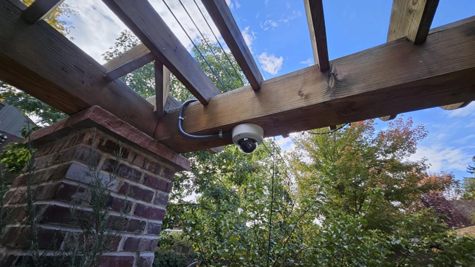 A security camera is hanging from the ceiling of a pergola.