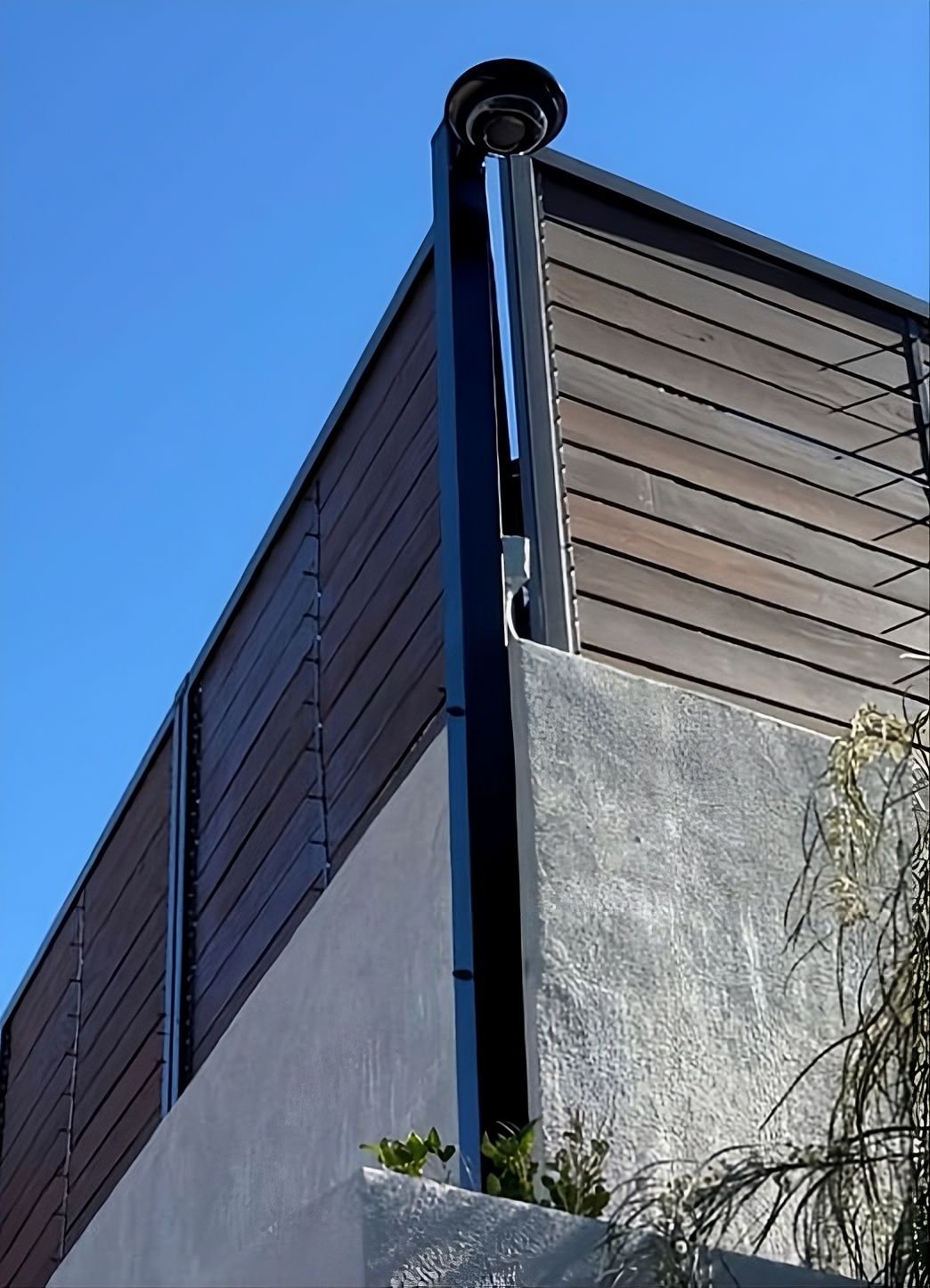 A security camera is mounted to a wooden post in front of a tree.