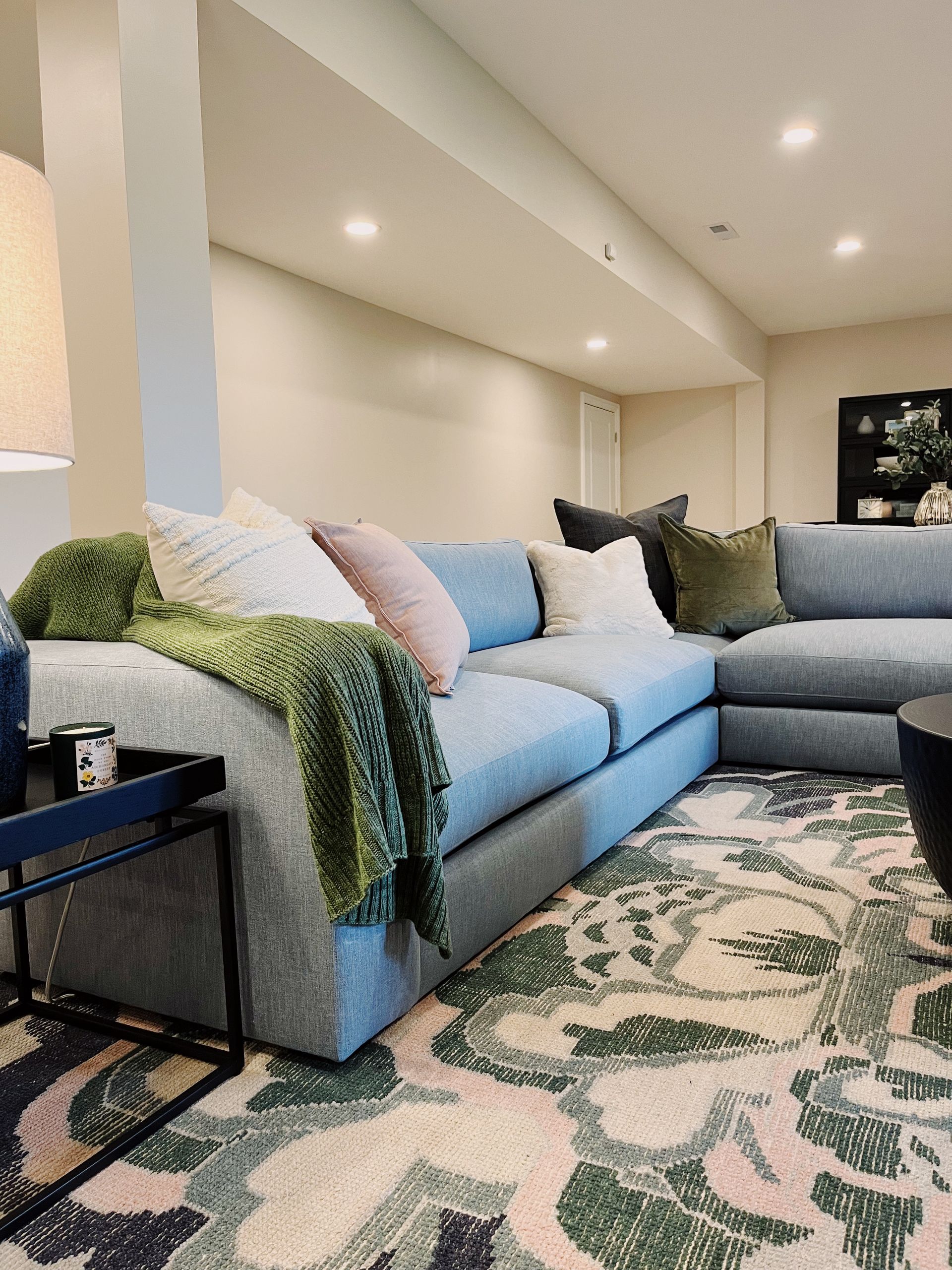 Cozy living room with a gray sectional, green throw, patterned rug, and recessed ceiling lights