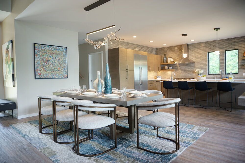 Modern open-plan dining and kitchen area with a round table, blue rug, and barstools by a bright island.