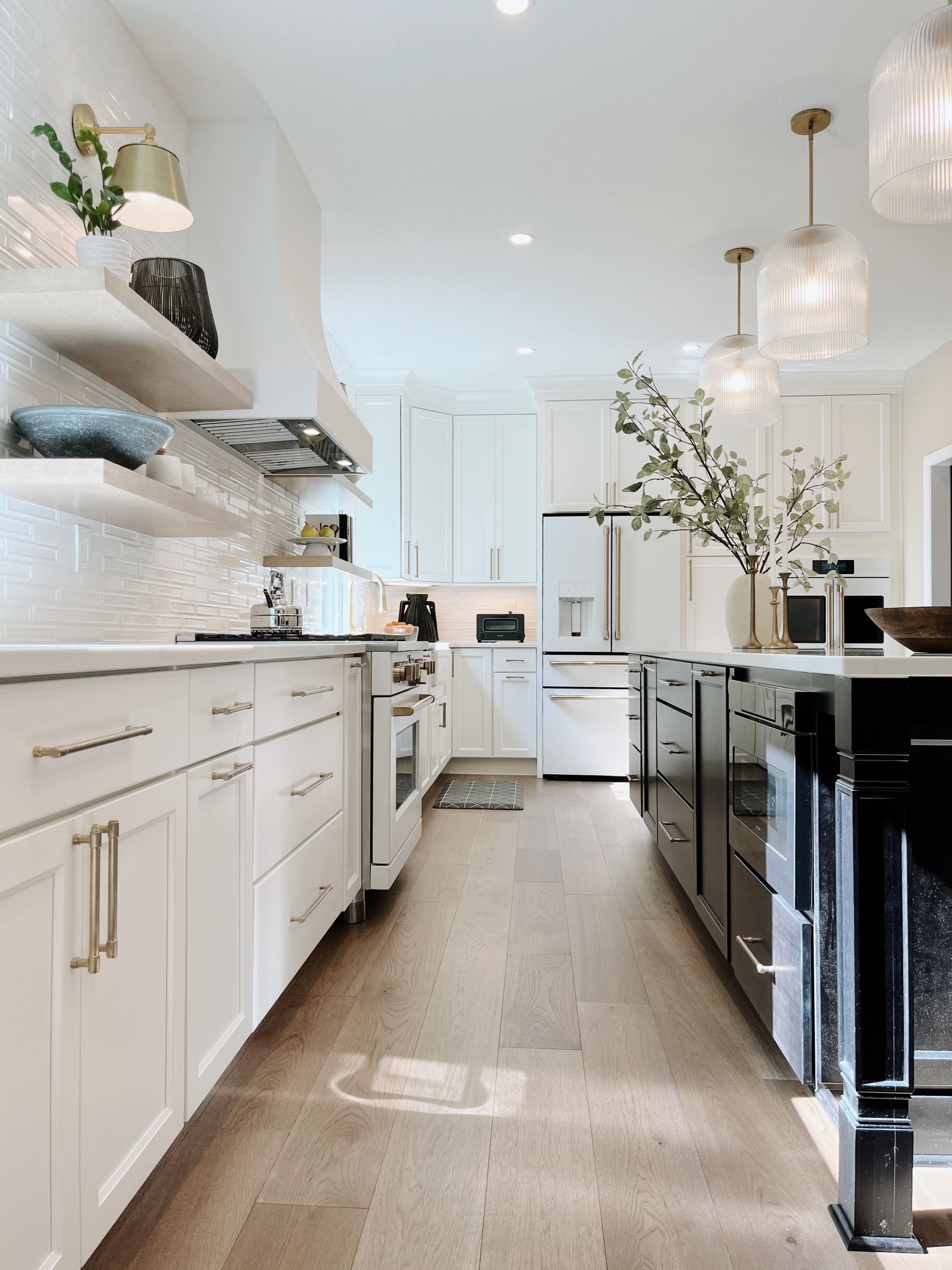 Bright white kitchen with black island cabinets, open shelves, and pendant lights