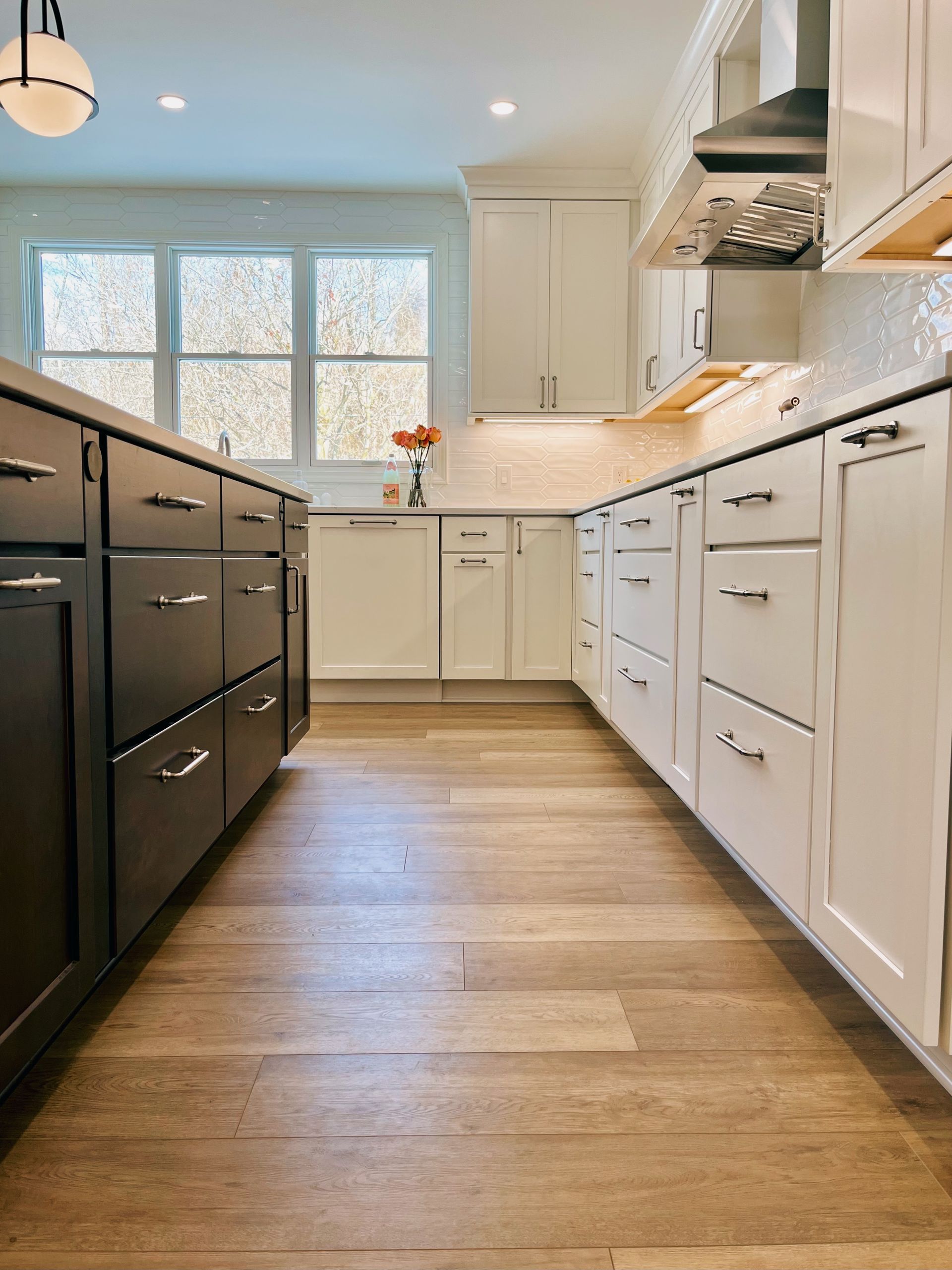 Modern kitchen with white and black cabinets, wood floor, and a bright window at the end