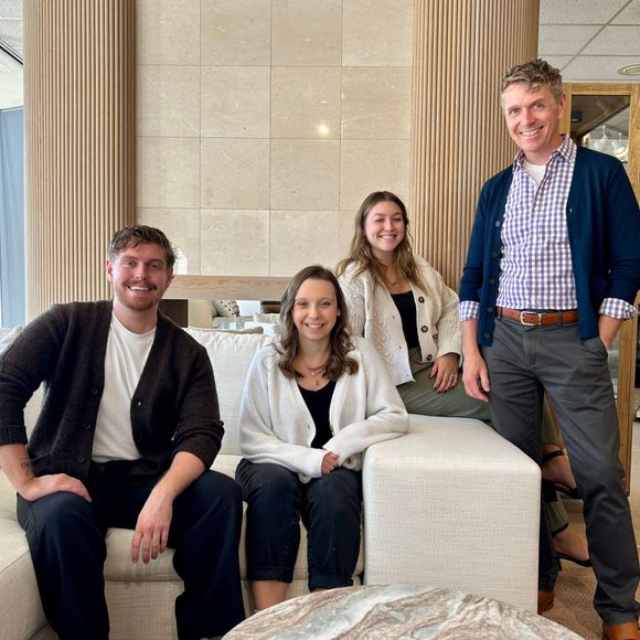 Four people pose together in a bright, modern office space with textured walls and neutral furniture.