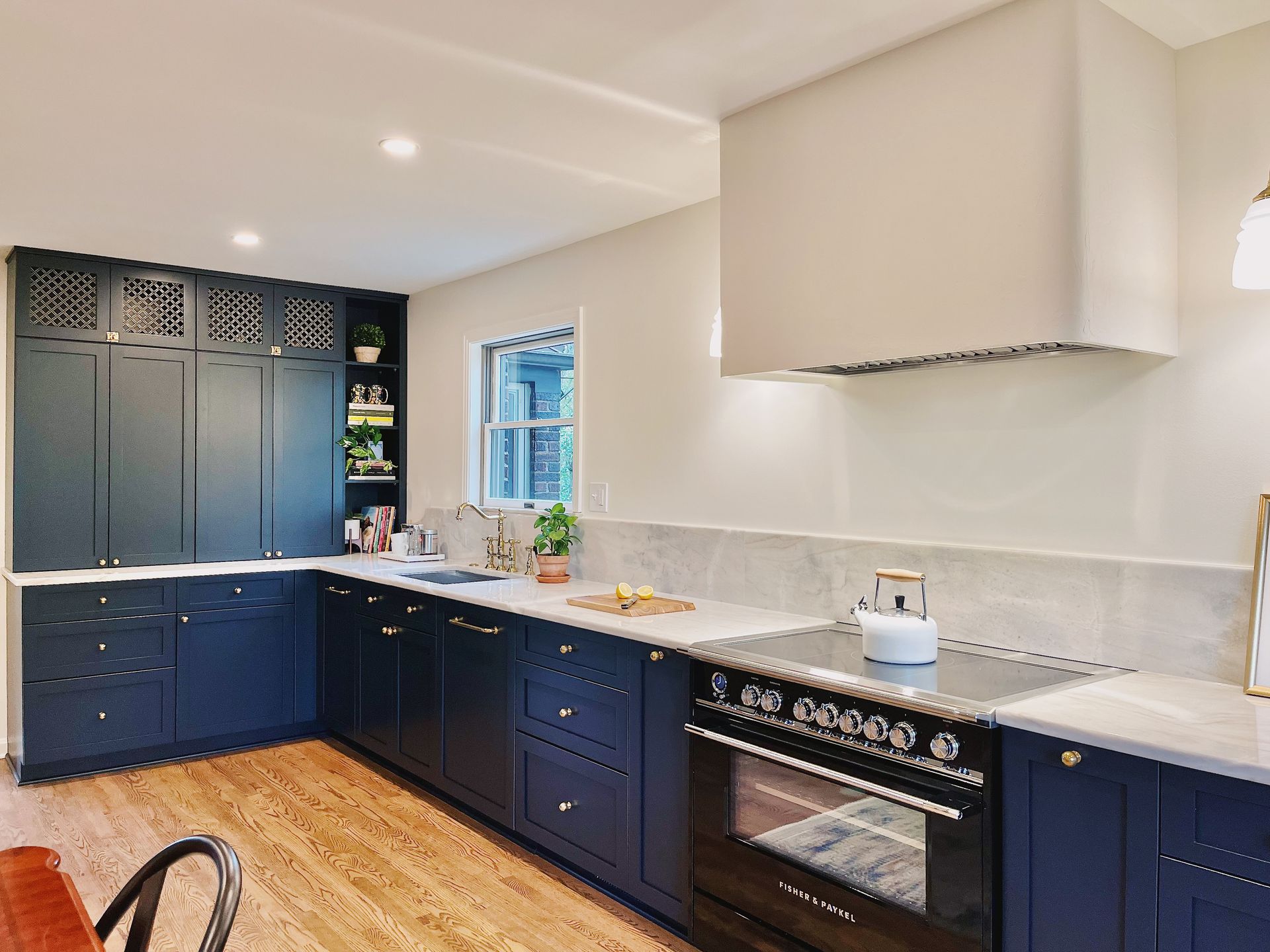 A modern kitchen with dark blue cabinetry, a white range hood, light countertops, and light-toned wood flooring.