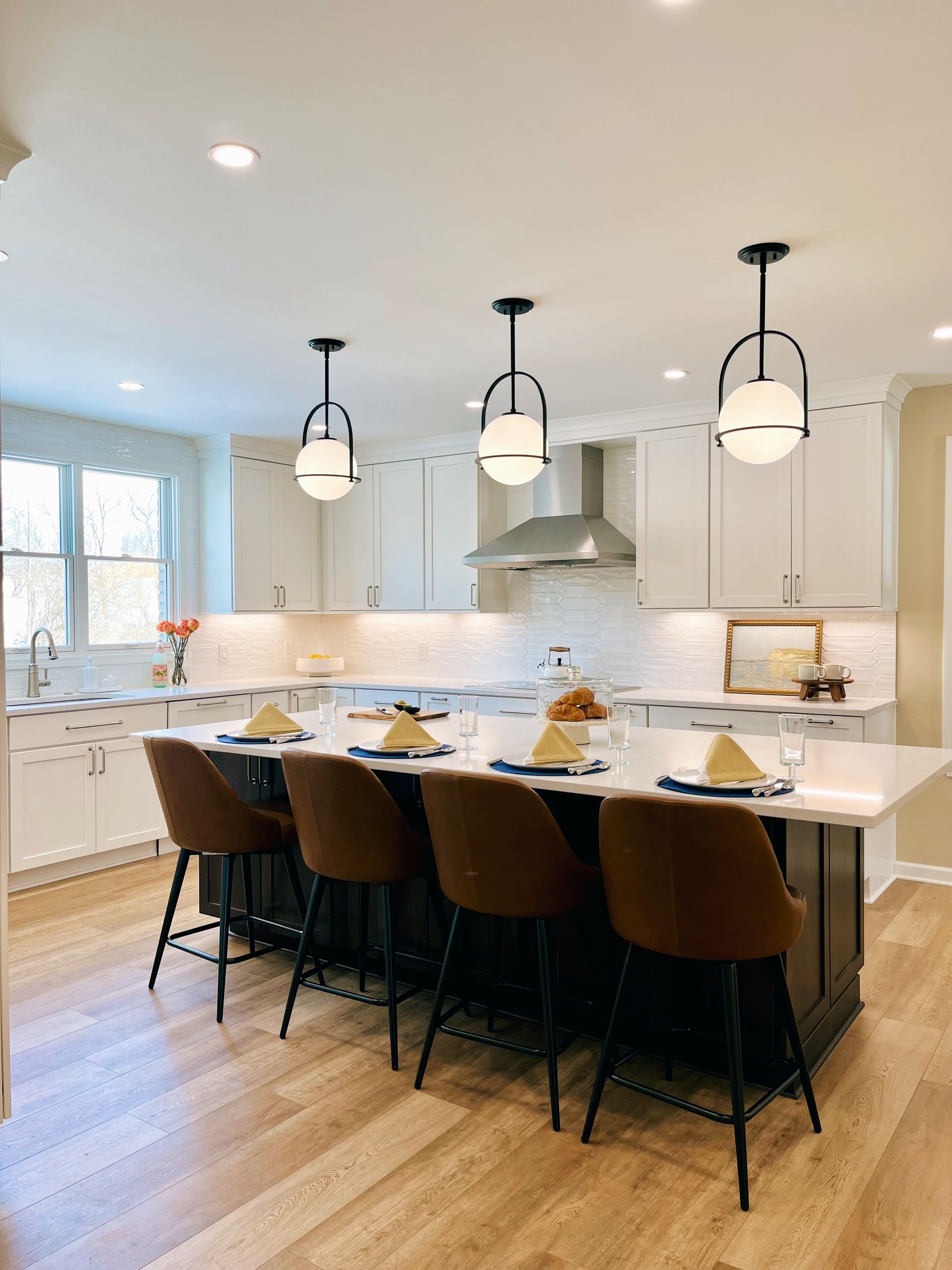 Modern kitchen with white cabinets, a dark island, light wood floors, and three hanging globe pendant lights.