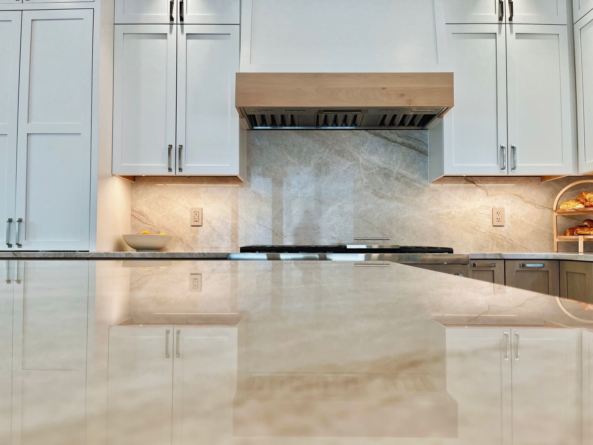 Modern kitchen with white cabinets, wood range hood, marble backsplash, and glossy countertop reflection