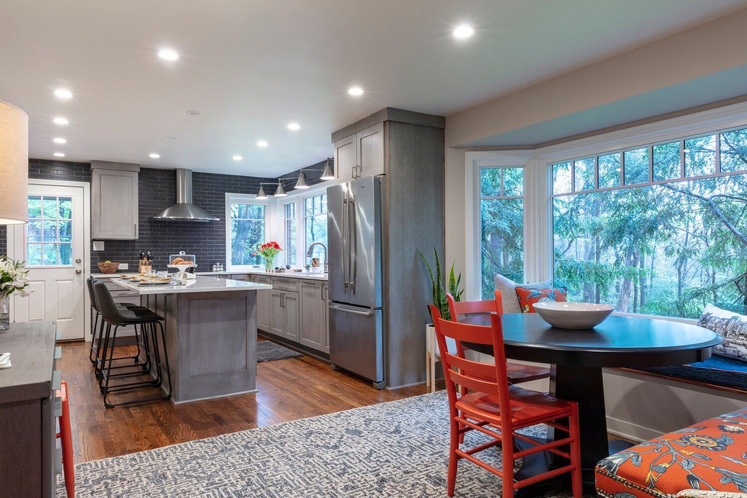 Modern kitchen and dining area with gray island, wood floors, and large bay window.
