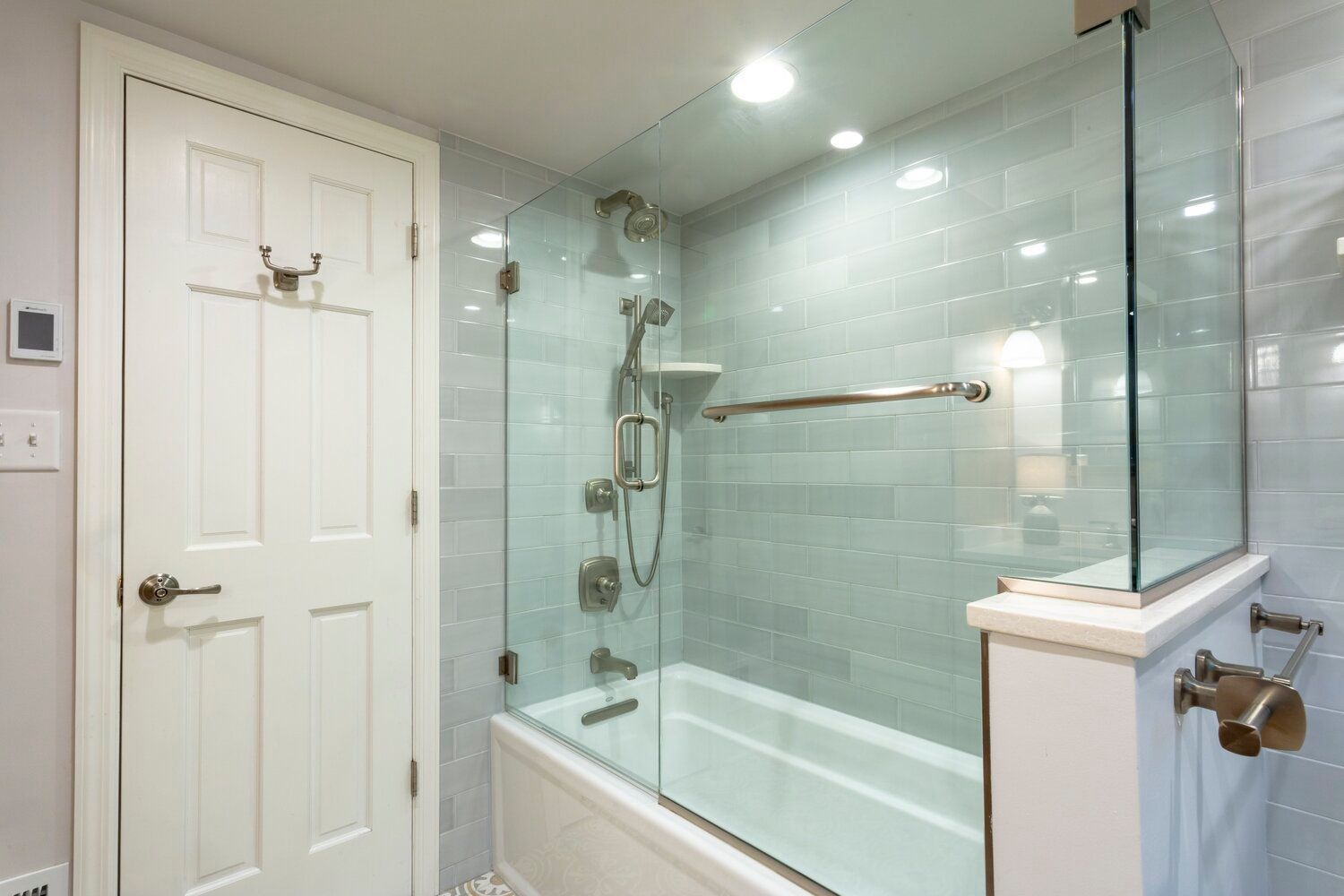 A white bathtub with a glass enclosure, silver shower fixtures, and tiled walls next to a closed white door.