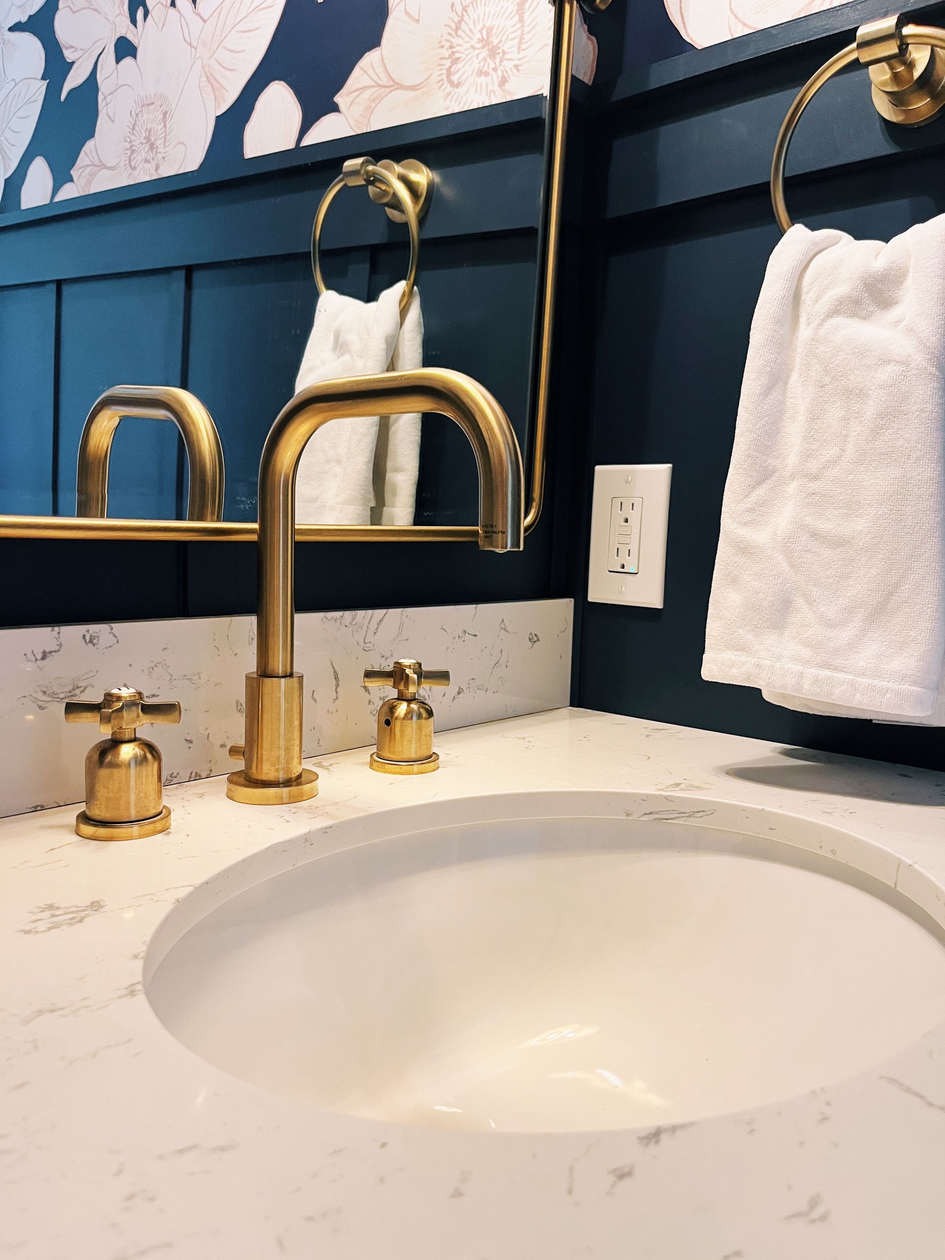 Bathroom vanity with a white marble countertop, brushed gold faucet and hardware, against a dark navy blue paneled wall.