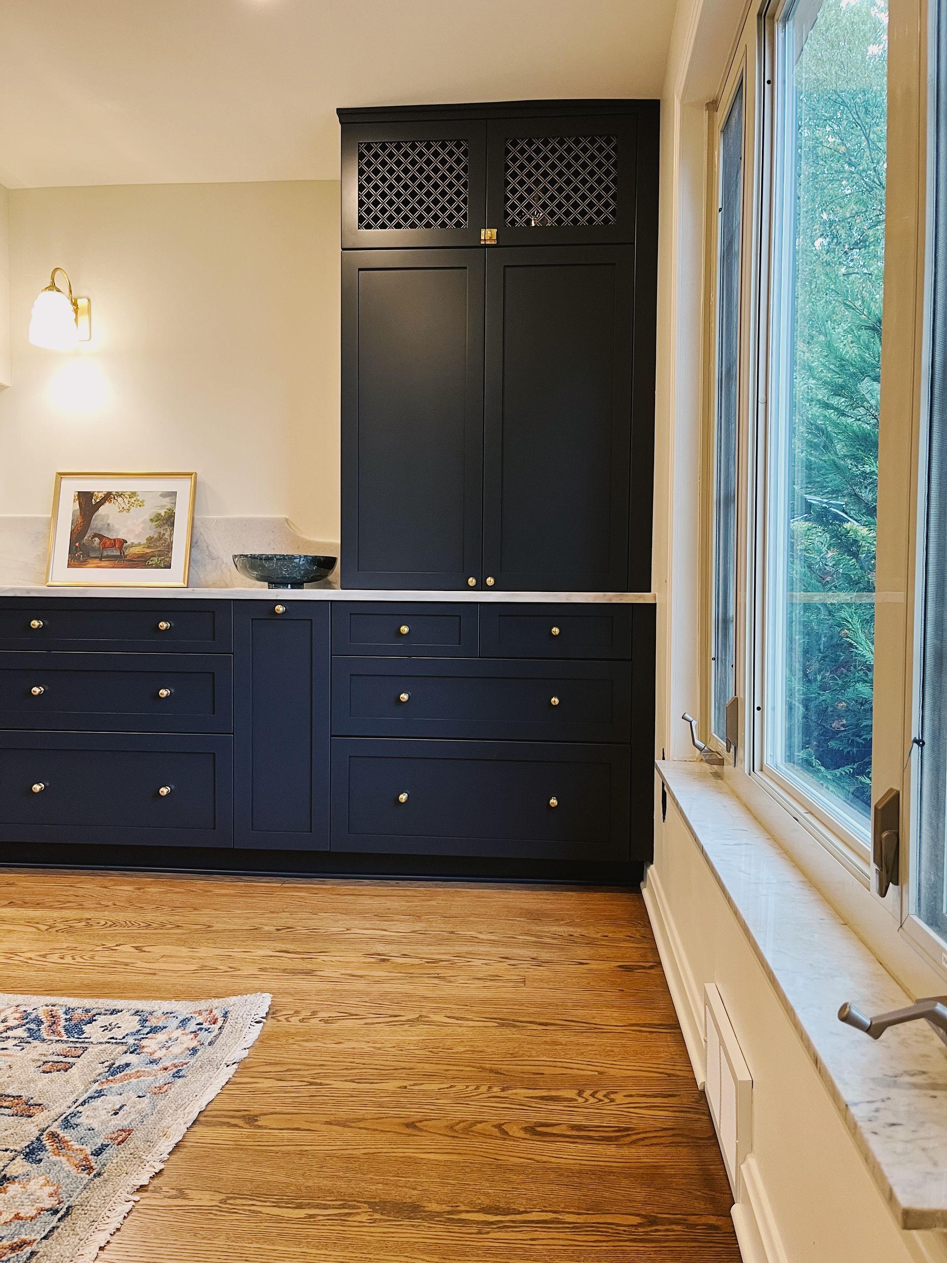 A modern kitchen corner featuring dark navy cabinets, a tall built-in pantry, light countertops, and wood flooring.