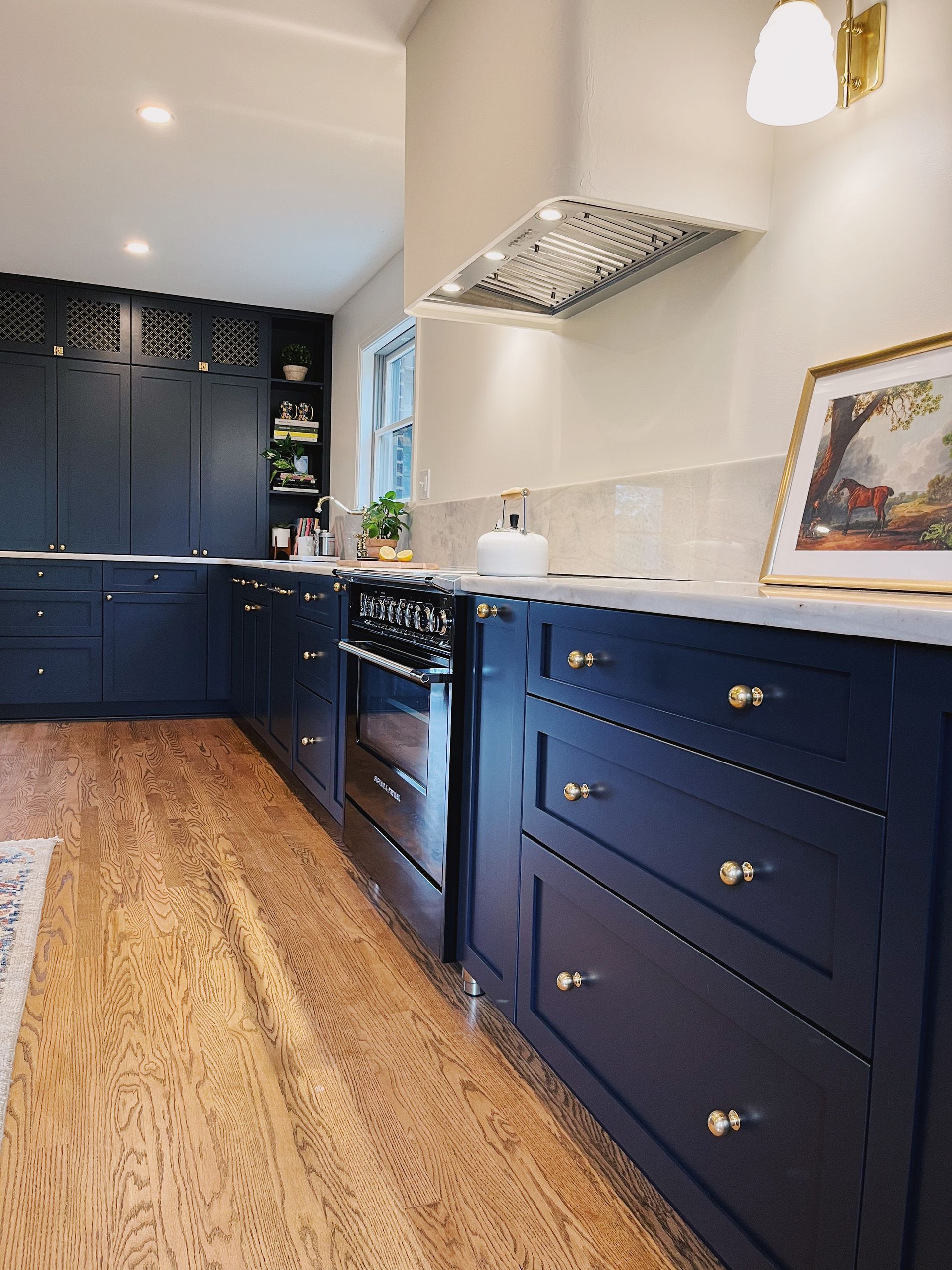 Navy blue galley kitchen with brass knobs, white tile backsplash, and wood floor.
