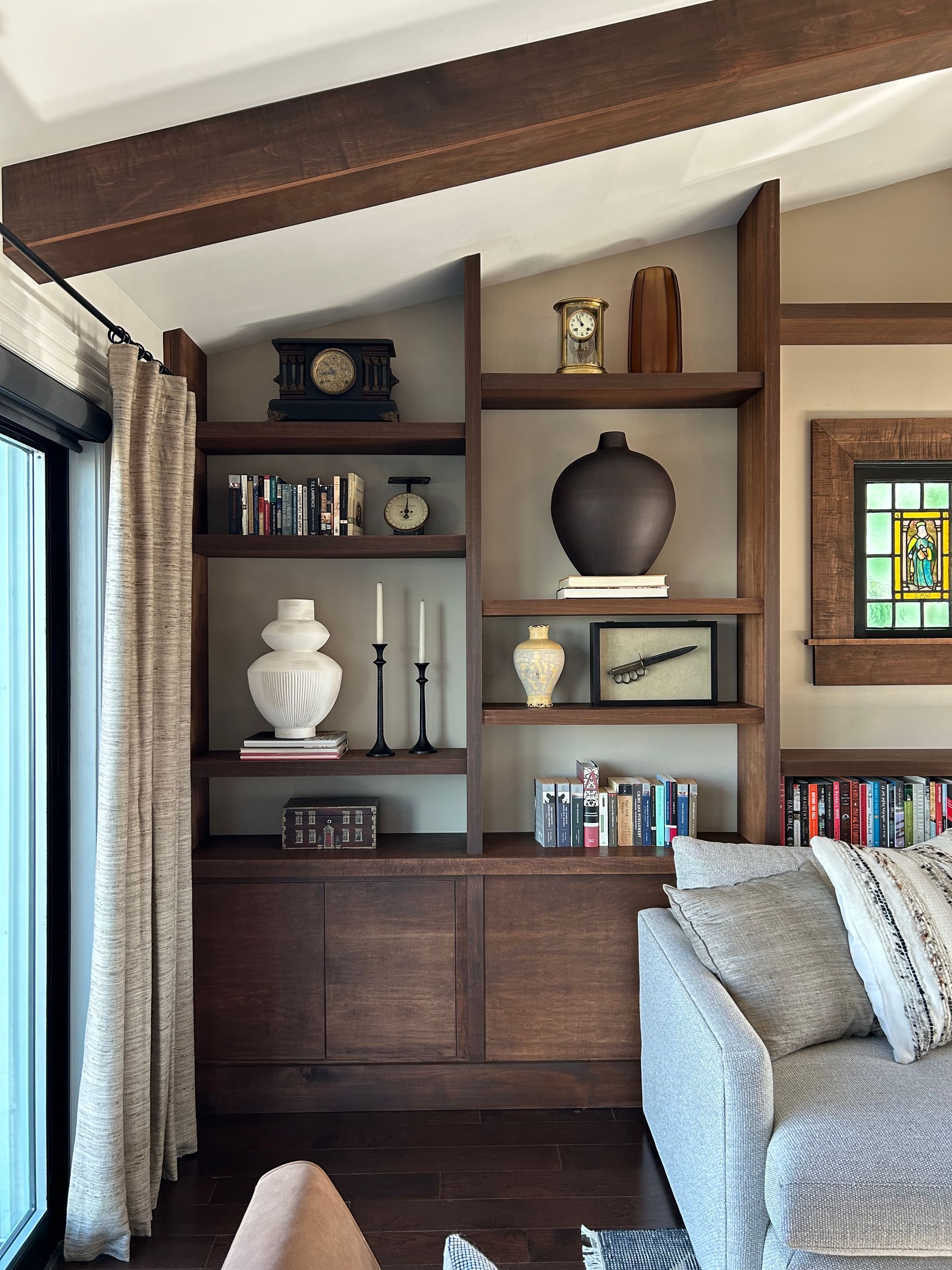 Built-in wooden shelves with books and decor beside a window, next to a gray sofa in a cozy room