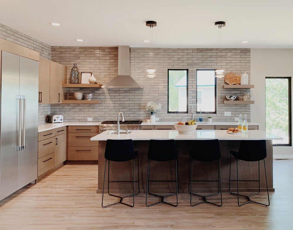 Modern kitchen with white island, black stools, wood cabinets, and light tile backsplash.
