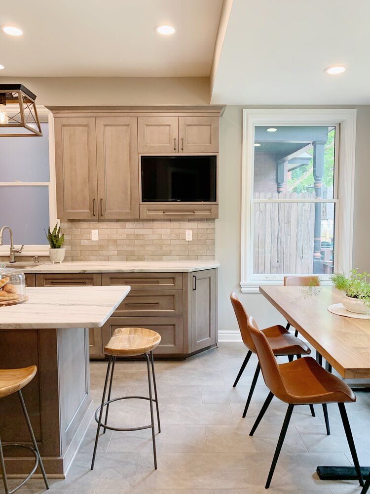 A modern kitchen with wood cabinets, light countertops, bar stools at an island, and a dining table with chairs.