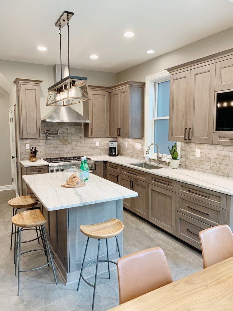 Modern kitchen with light wood cabinets, white stone countertops, a central island with stools, and pendant lighting.