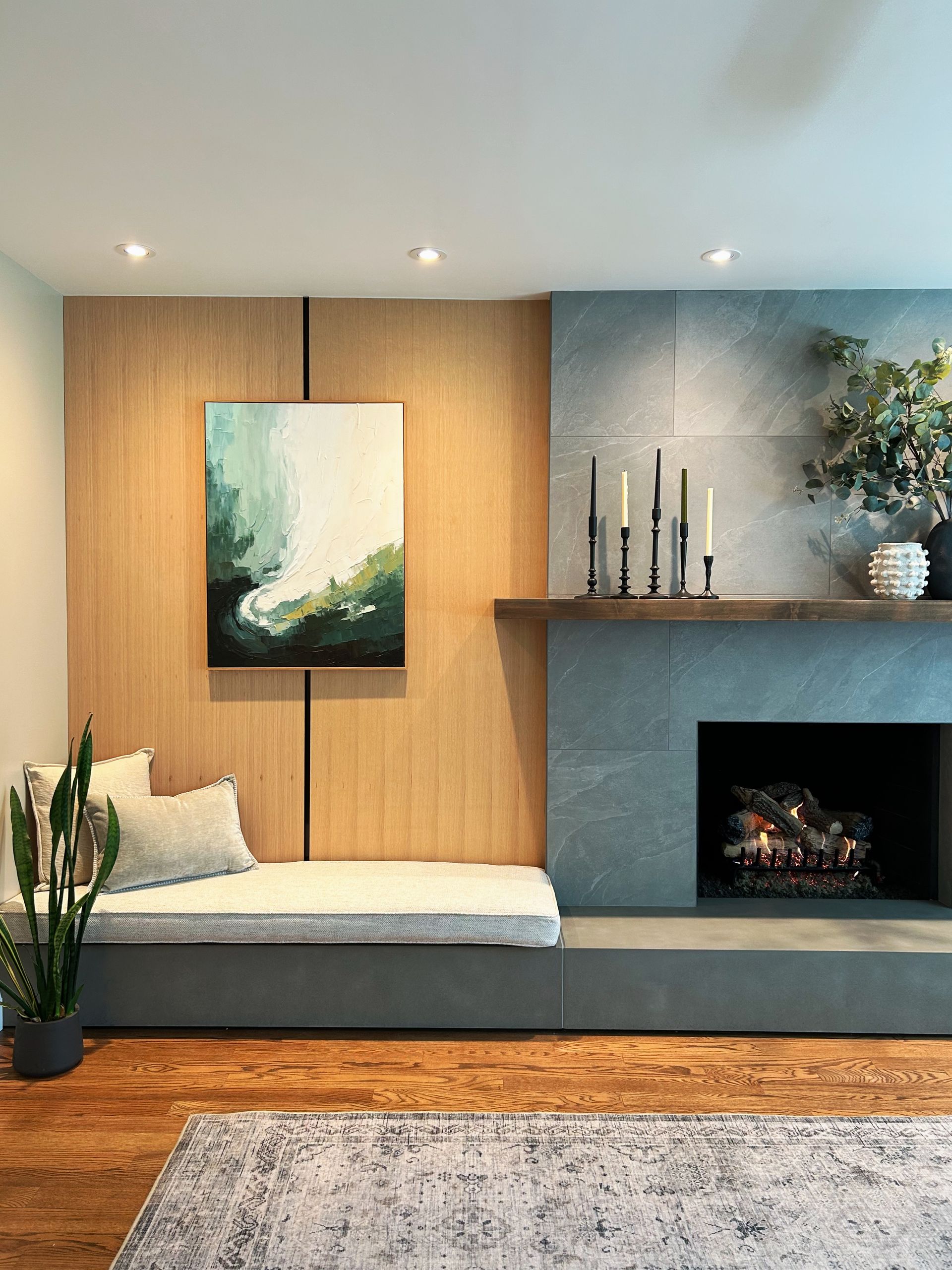 Modern living room with wood-paneled bench, fireplace, abstract art, plants, and a gray rug.