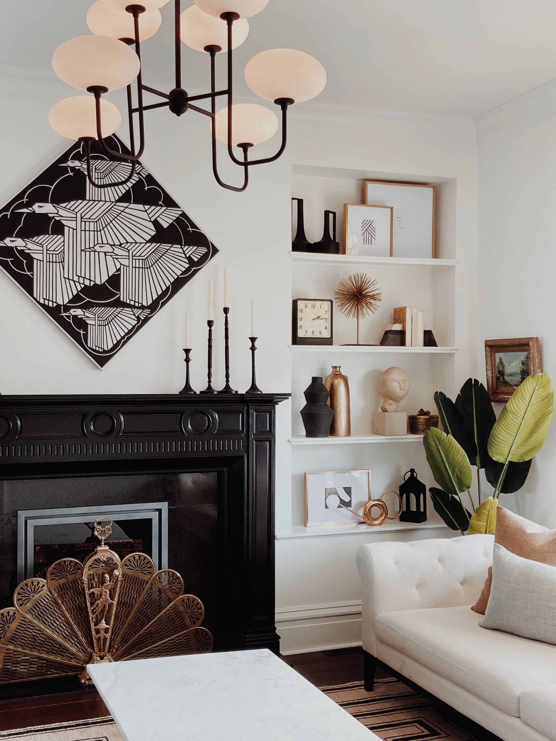 Cozy living room with black fireplace, white shelves, chandelier, and cream sofa with greenery