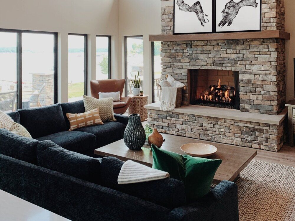 Modern living room with black sofa, stone fireplace, and large windows overlooking a city view