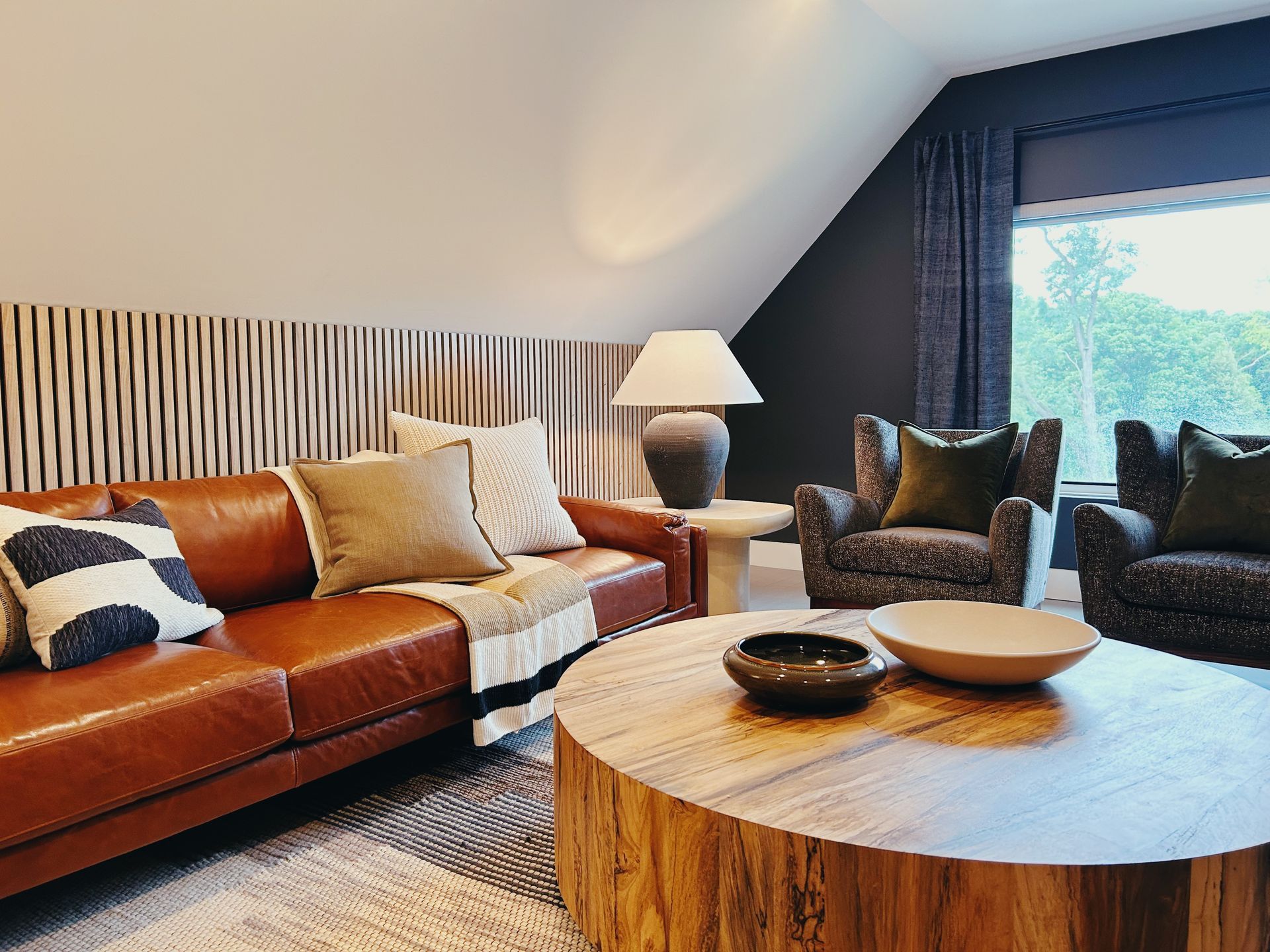 Cozy living room with leather sofa, patterned chairs, round wood coffee table, and sloped ceiling