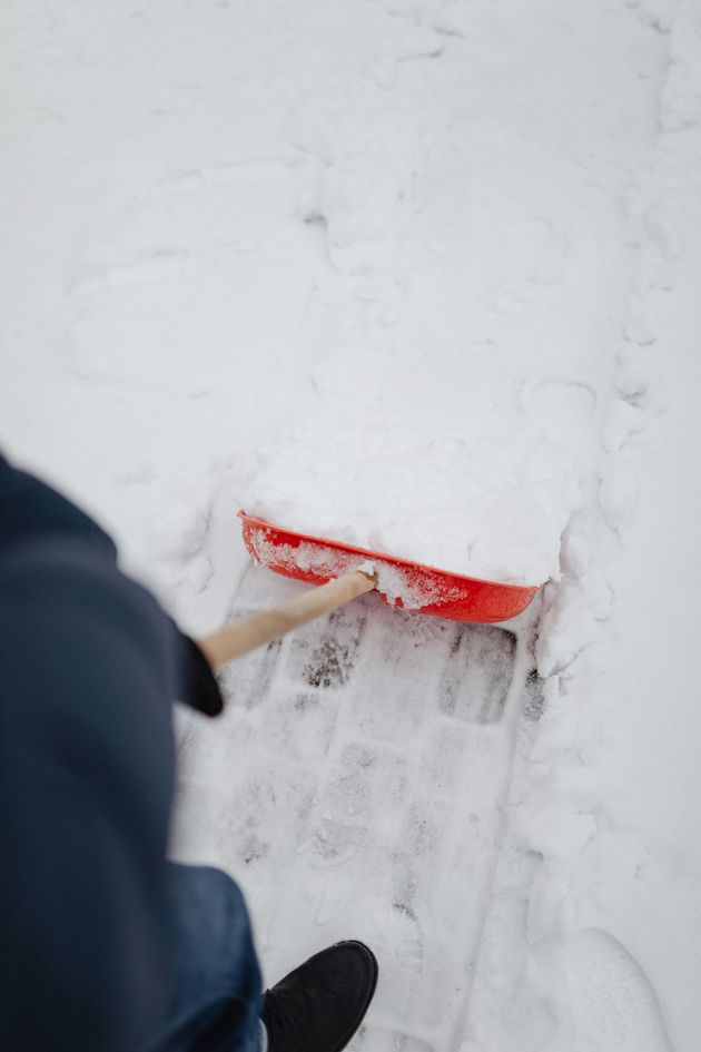 A person is shoveling snow on a sidewalk with a red shovel.