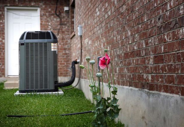 An air conditioner is sitting on the side of a brick building next to a flower.