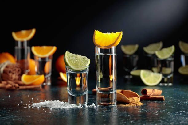 Two glasses of tequila with slices of orange and lime on a table.