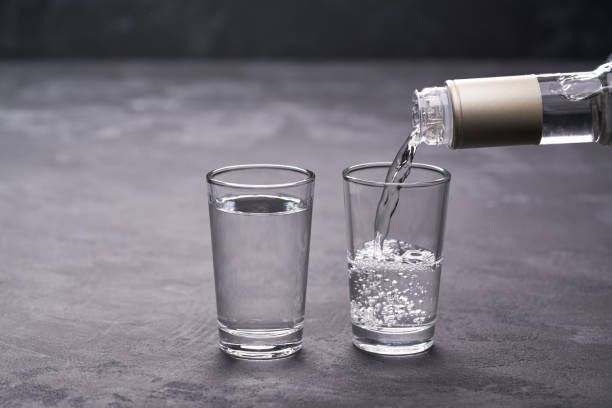 A bottle of vodka is being poured into two shot glasses.