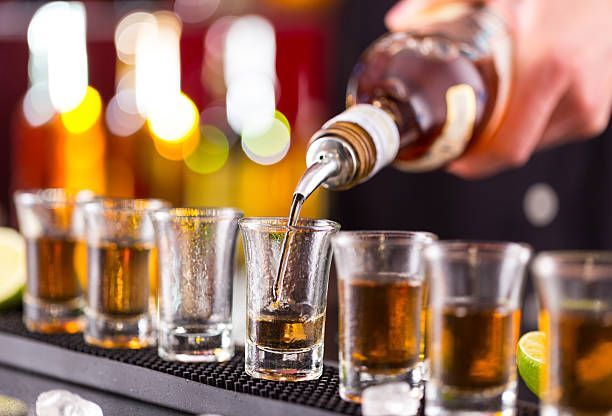 A bartender is pouring tequila into shot glasses on a bar.