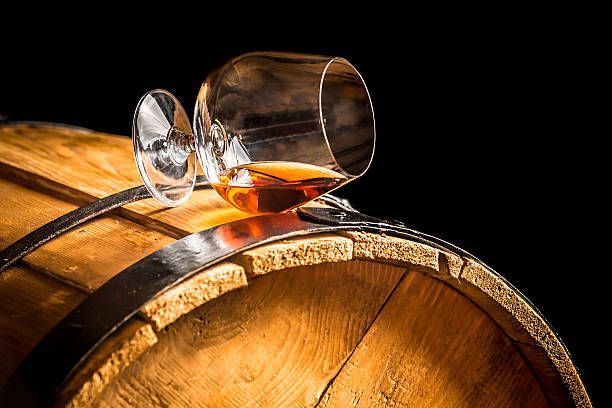 A glass of cognac is sitting on top of a wooden barrel.