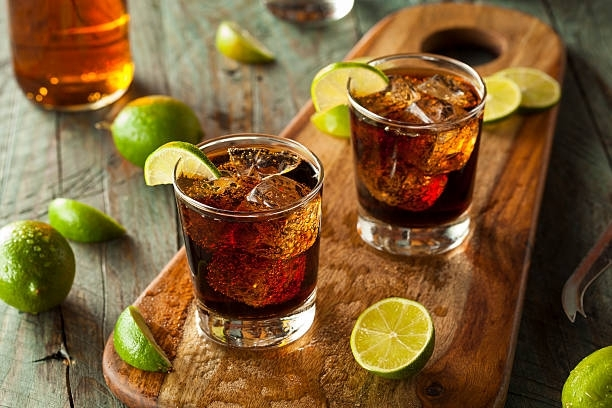 Two glasses of cola with ice and lime slices on a wooden cutting board.