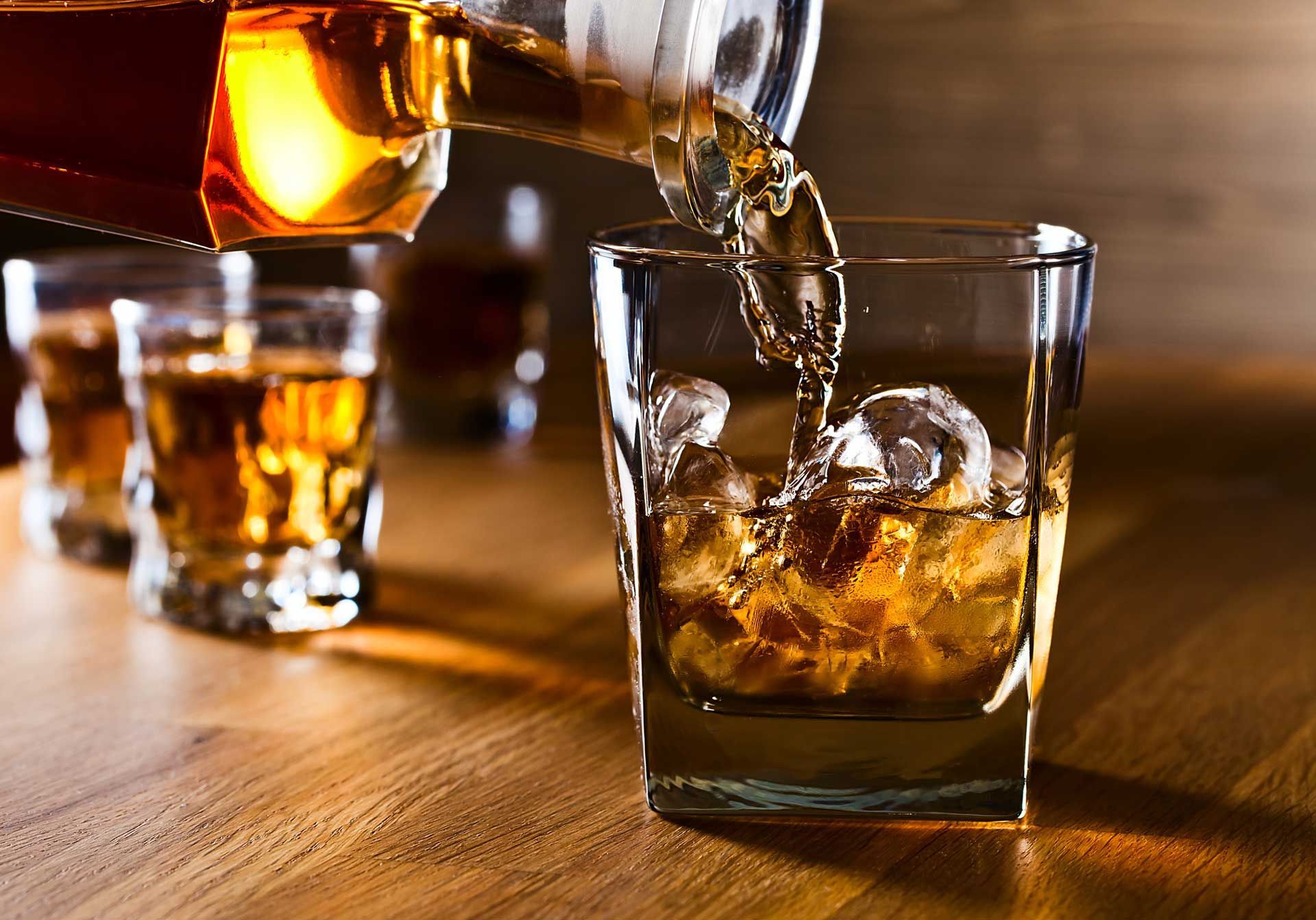 A bottle of whiskey is being poured into a glass with ice.